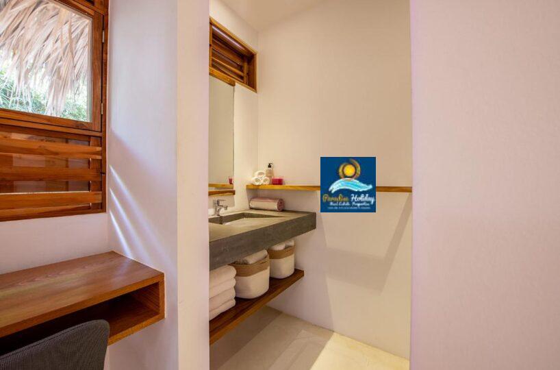 Baño en Las Terrenas con accesorios modernos, lavabo de concreto y espacio de almacenamiento con toallas.