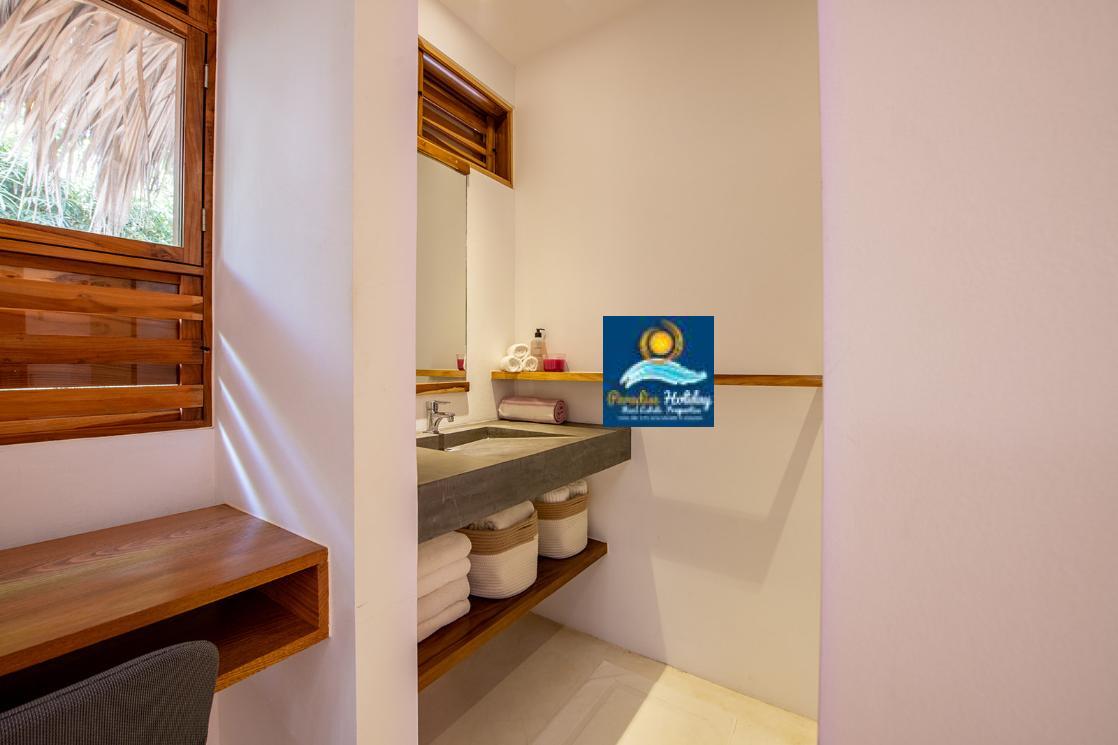 Baño en Las Terrenas con accesorios modernos, lavabo de concreto y espacio de almacenamiento con toallas.