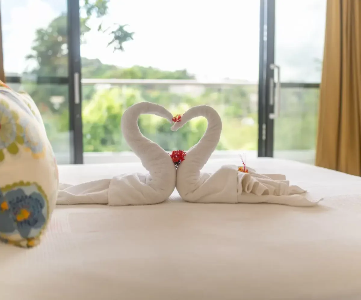 Toallas en forma de cisnes en la cama con vista a la terraza y naturaleza.