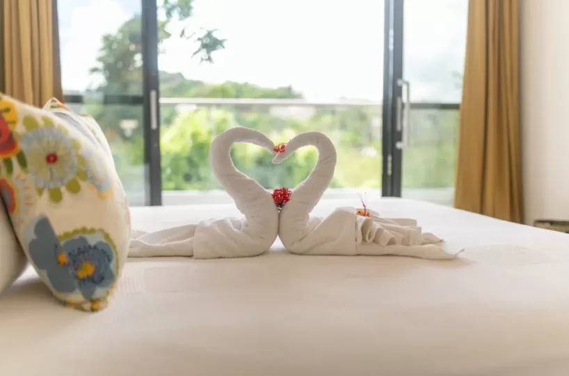 Toallas en forma de cisnes en la cama con vista a la terraza y naturaleza.
